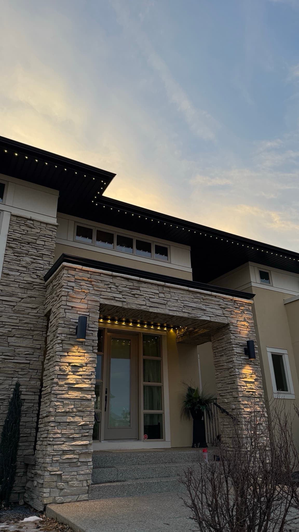 Angled front elevation at dusk with warm white permanent lighting.