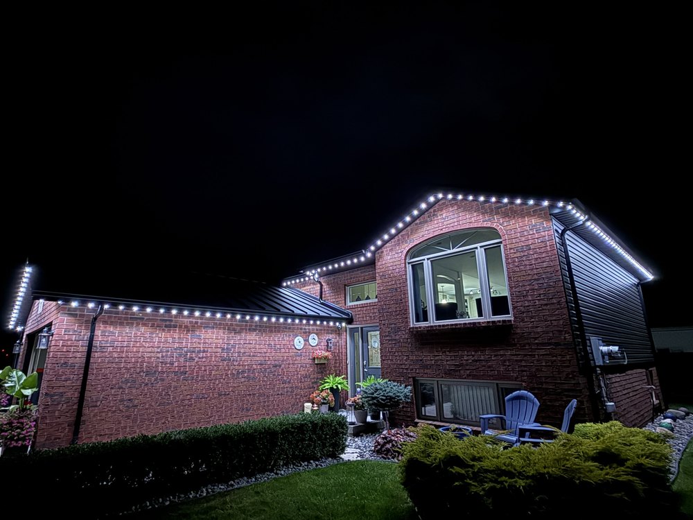 Cool white Luminair lighting along every roofline of a brick home at night, lighting the driveway, front walk and entry from above