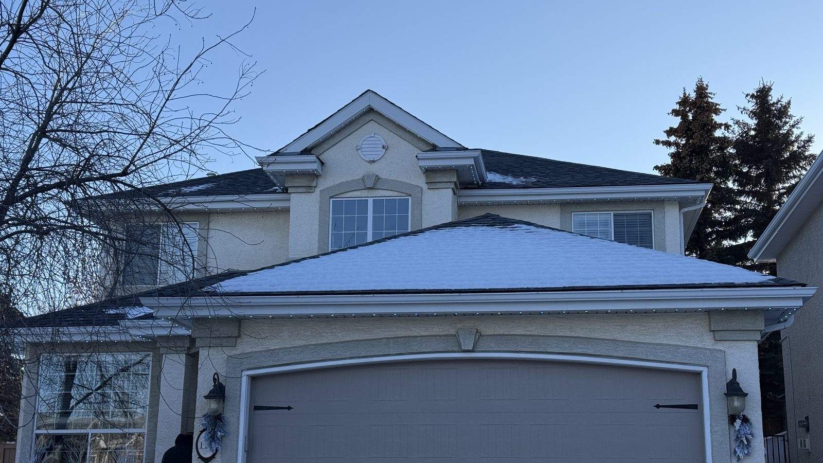 Cool white permanent lighting picking out the rooflines and centre dormer of a cream stucco two-storey at dusk