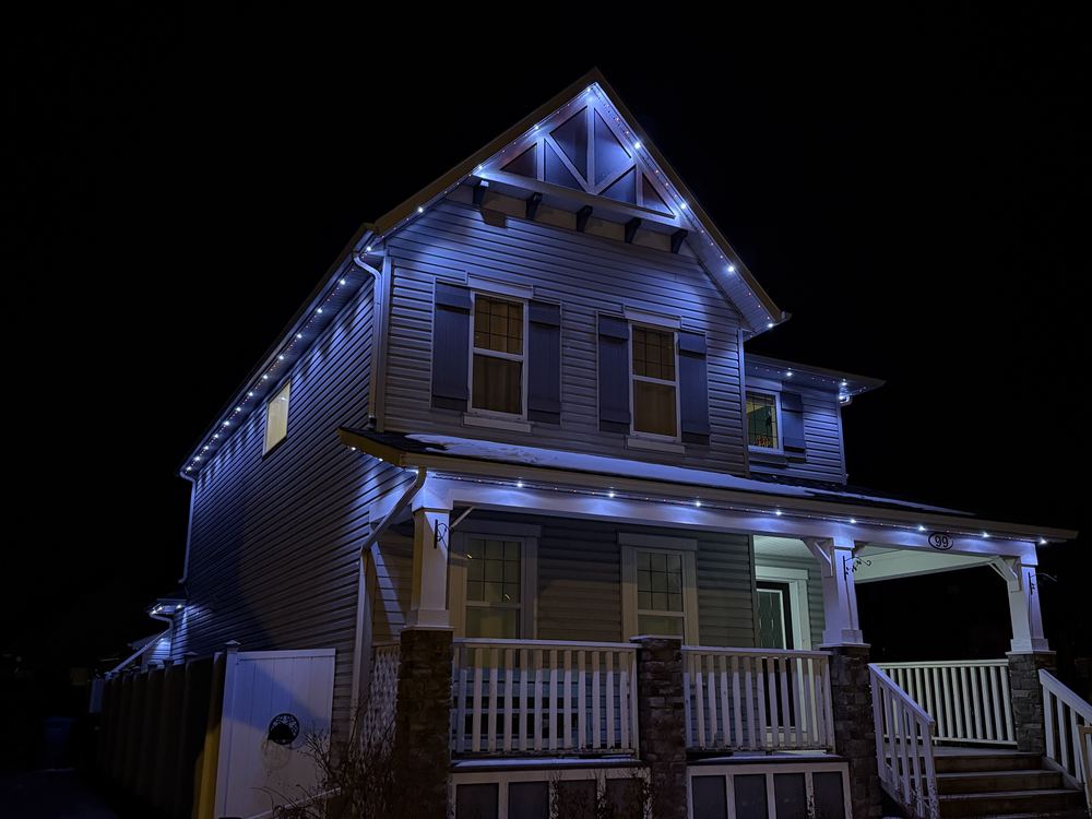 A craftsman home with blue and white Luminair lighting following the gable, eaves and porch