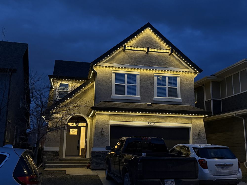 A gabled stucco home outlined in warm white Luminair lighting at dusk