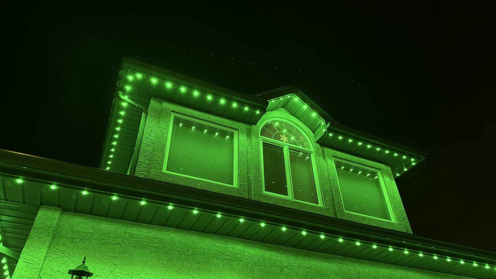 A green scene running along the gable, dormer and window trim of a stucco home at night