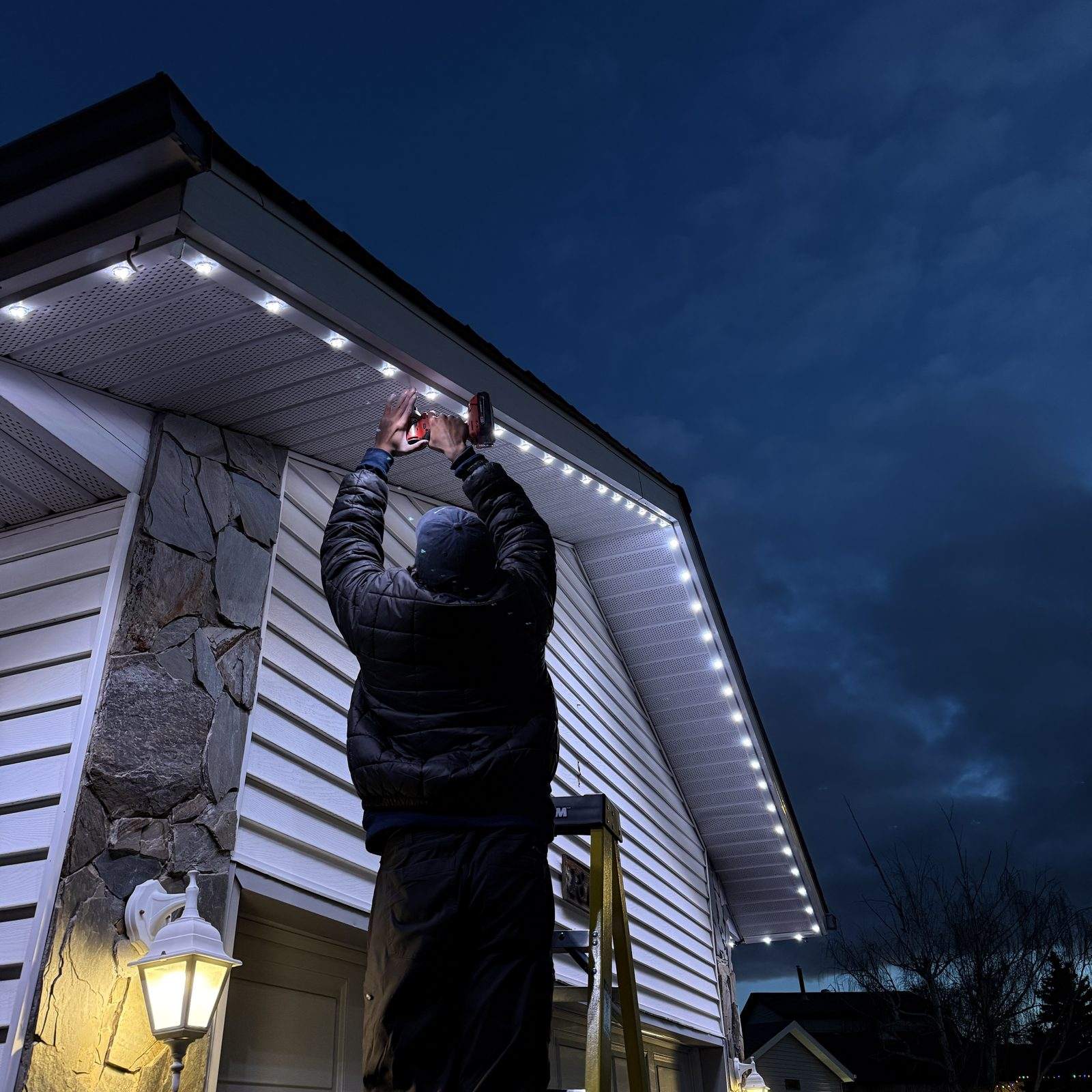 A Luminair installer fitting colour-matched track under the soffit at dusk, the finished run beside him already lit cool white
