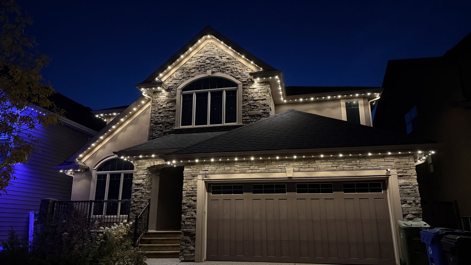 Luminair architectural warm white soffit lighting on a stone two-storey home in Calgary at dusk