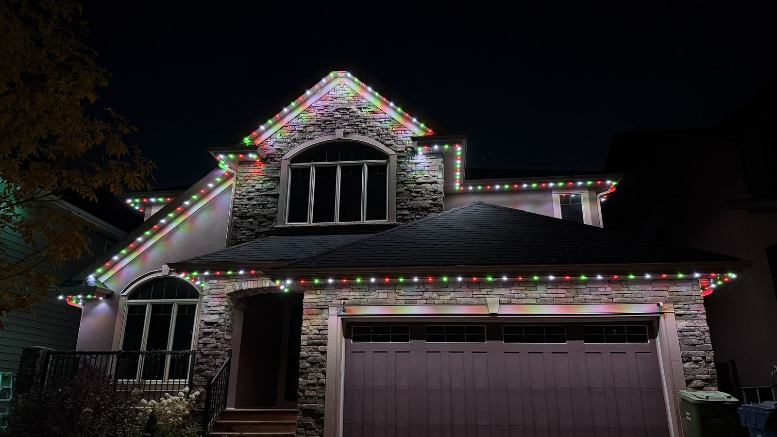 Luminair permanent Christmas lights in Calgary running a red, green and white scene along the roofline of a stone home