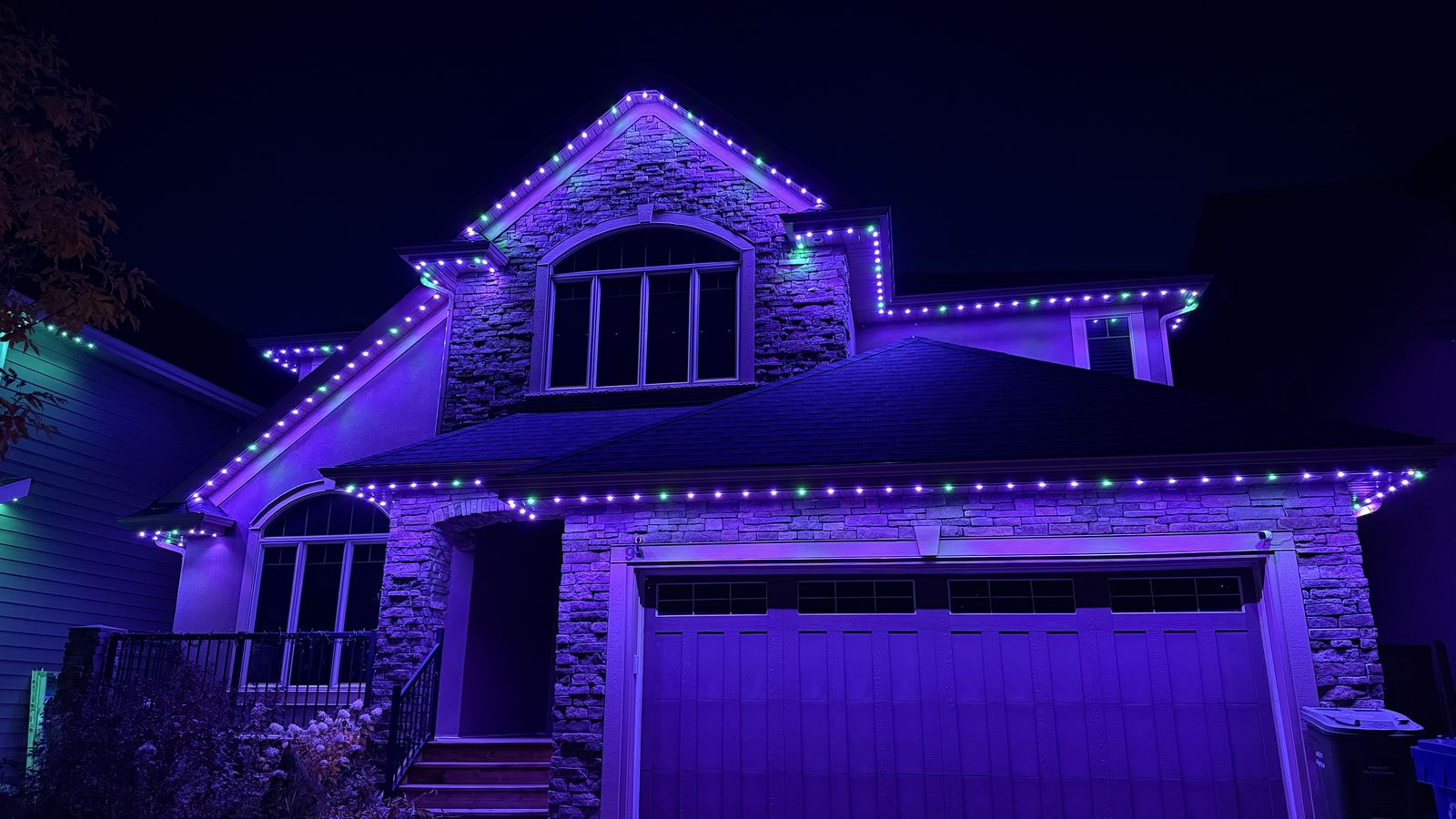 Luminair permanent soffit lights in Calgary set to purple and green for Halloween on a stone two-storey home