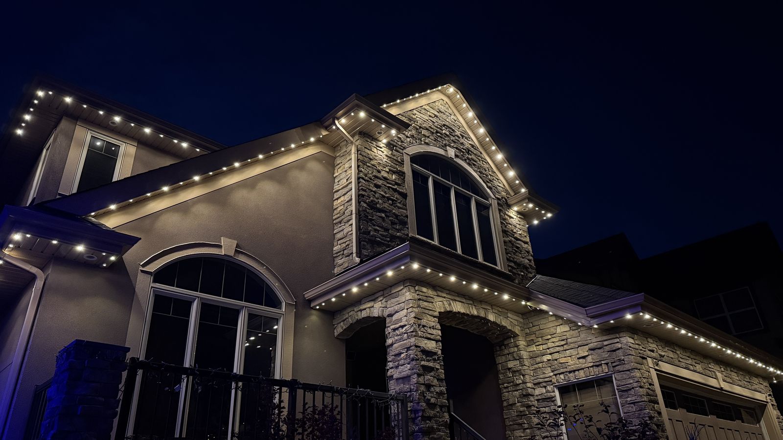 Angled view of Luminair warm white permanent lights tracing the gables and stone entry of a Calgary home