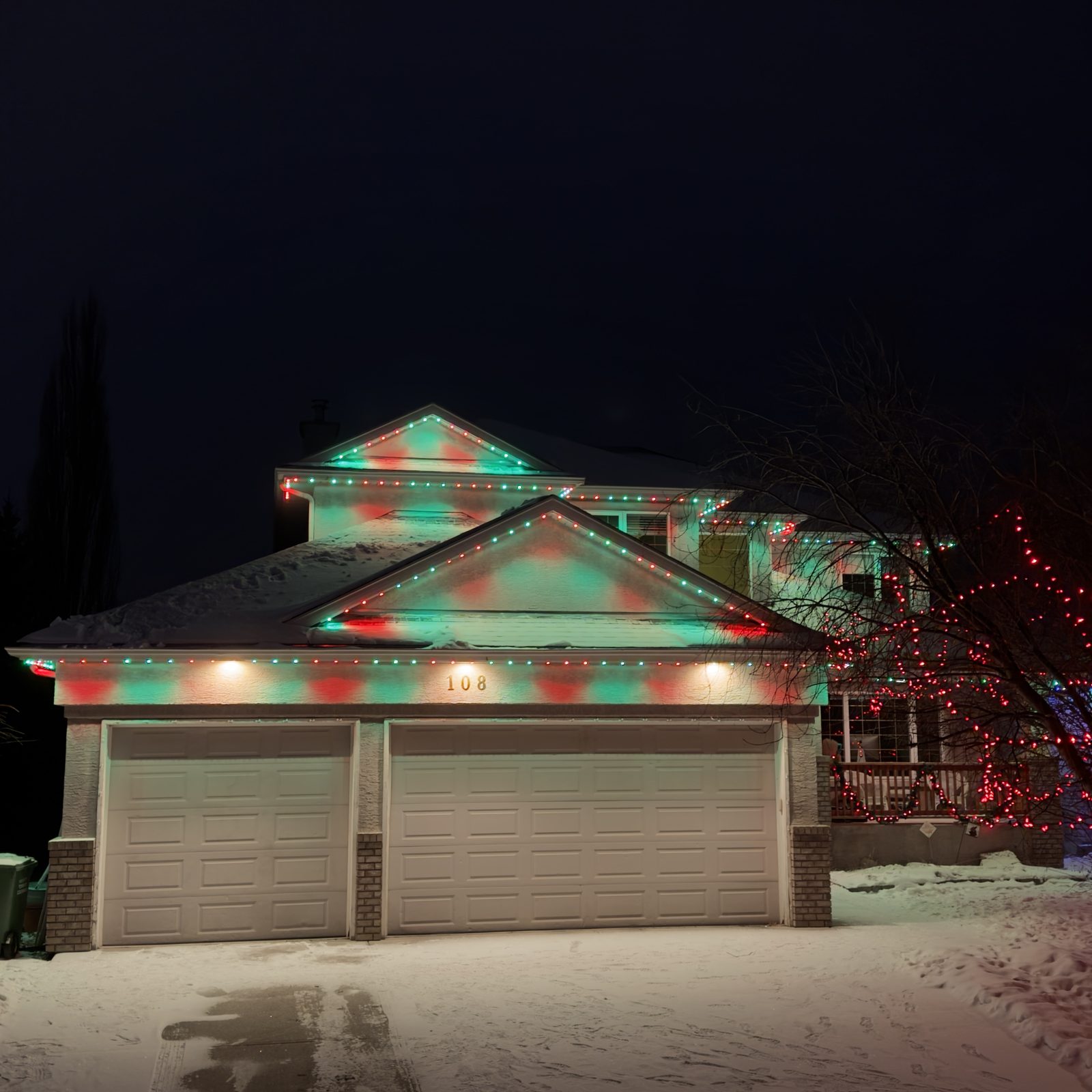 Permanent Christmas lights alternating red and green across the gables and double garage of a two-storey home in the snow
