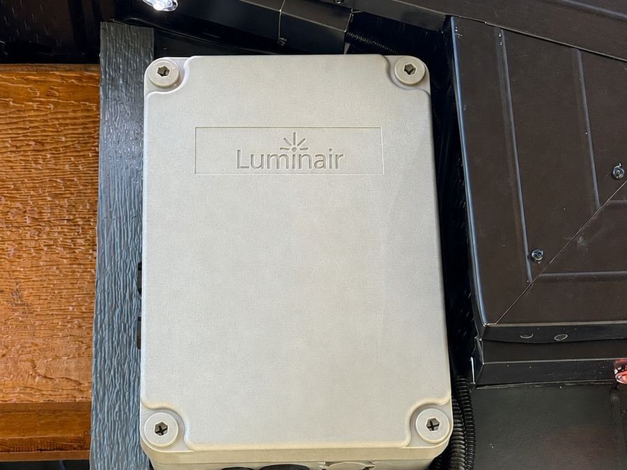 The weather-sealed Luminair smart controller mounted under a soffit with conduit runs into the housing