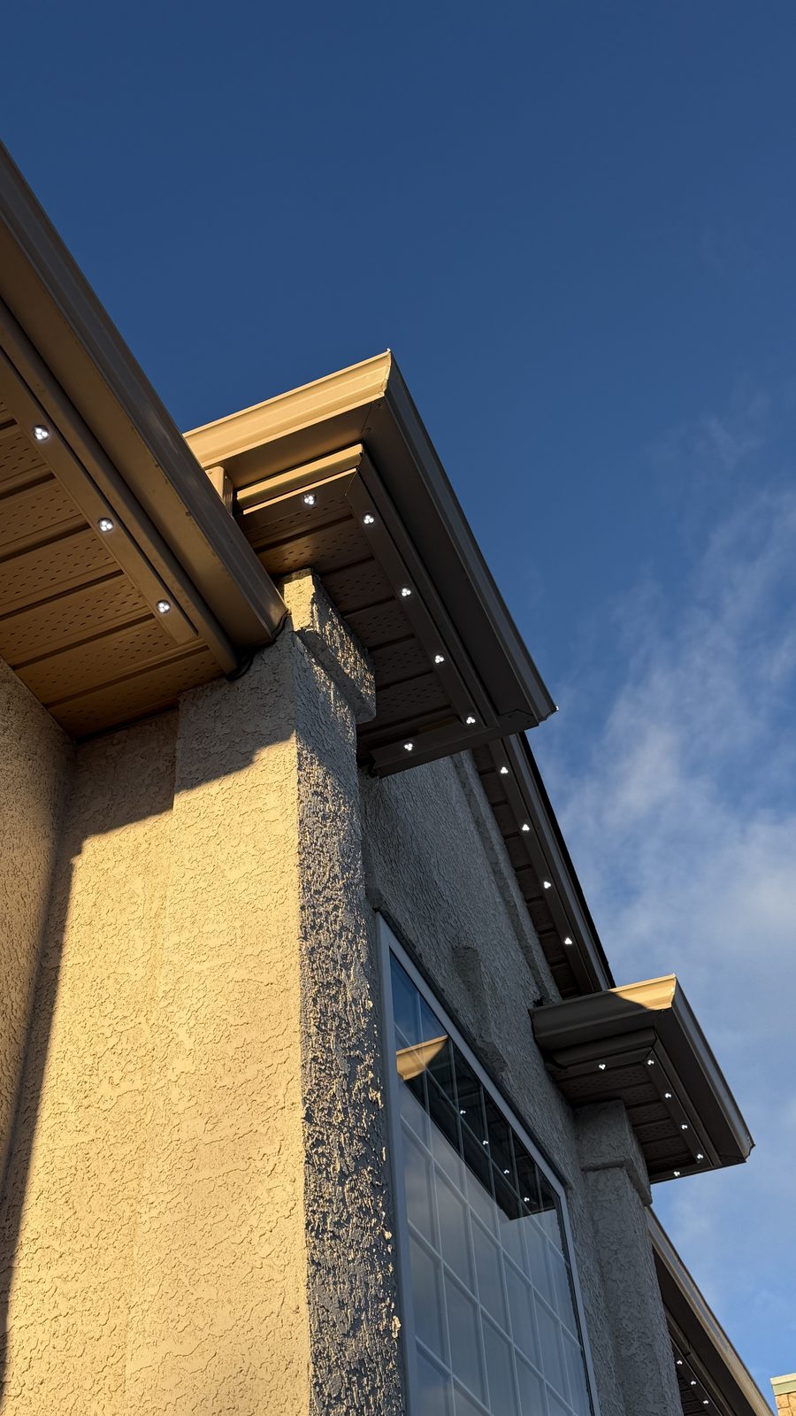 Close-up of Luminair track colour-matched to a tan soffit and brown fascia in daylight, the sealed fixtures sitting flush in the channel