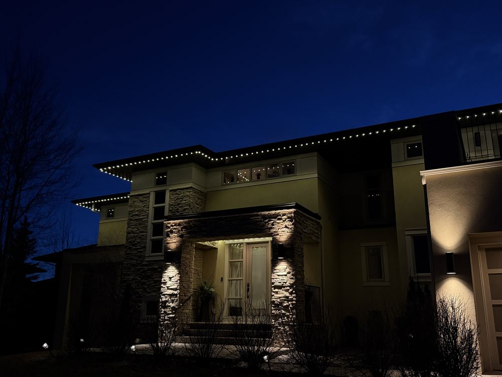 Twilight exterior of a modern home with Luminair roofline lighting and a lit stone entry