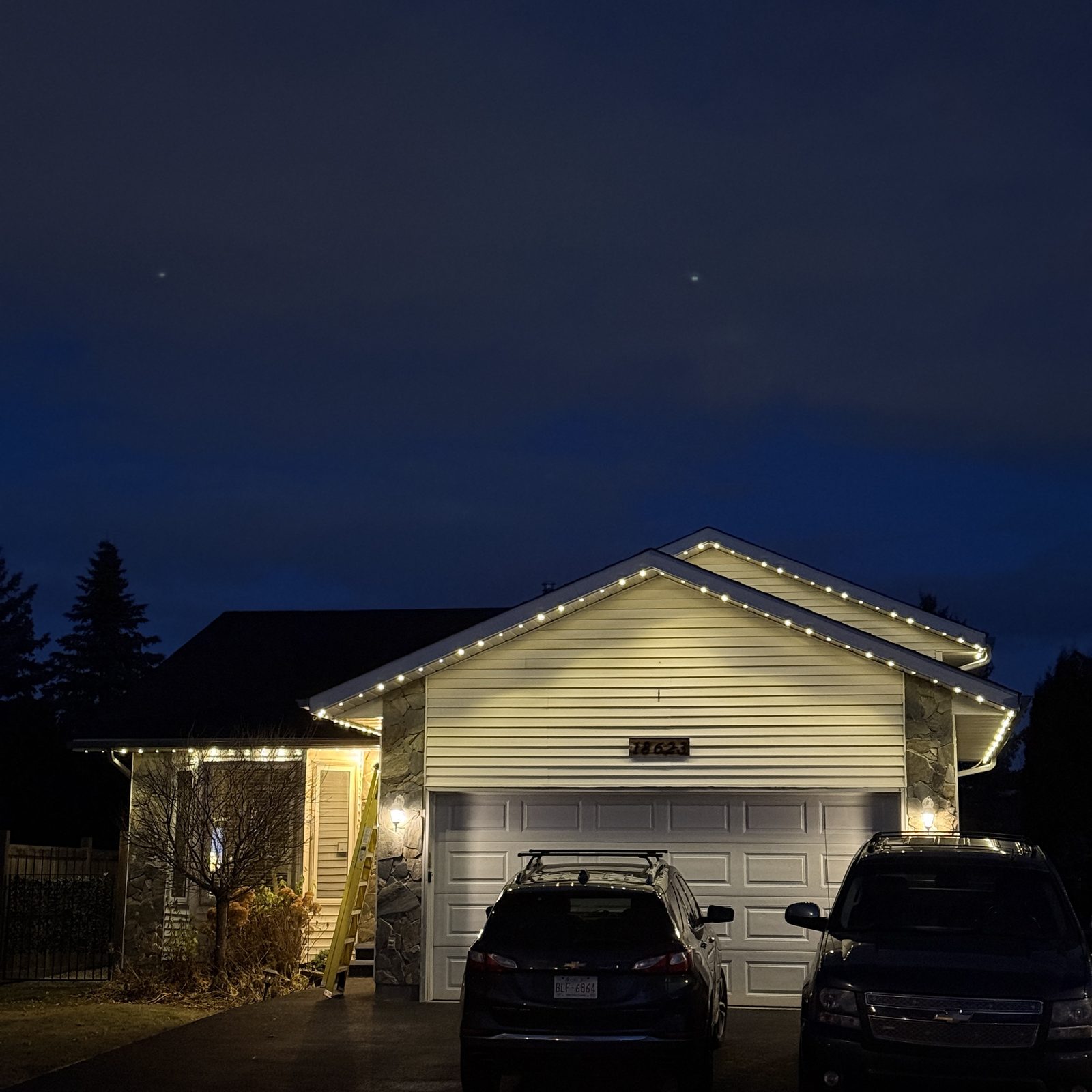 Warm white permanent lighting outlining the gable and eaves of a bungalow, with the driveway and garage lit below