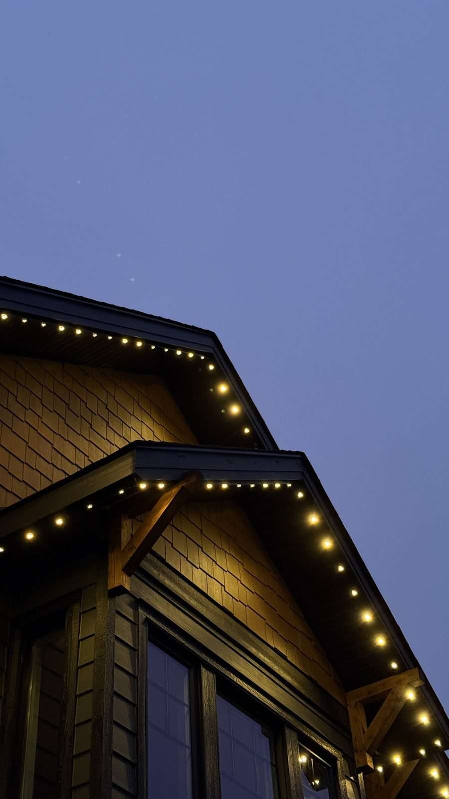 Close-up of warm white Luminair fixtures spaced evenly along a cedar-shingled gable with exposed timber brackets