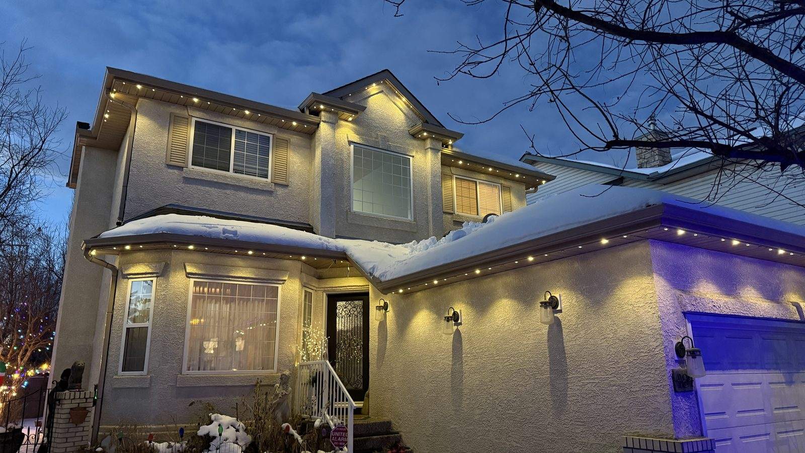 A stucco two-storey lit warm white along every roofline with the garage bay set to purple, showing per-zone colour control